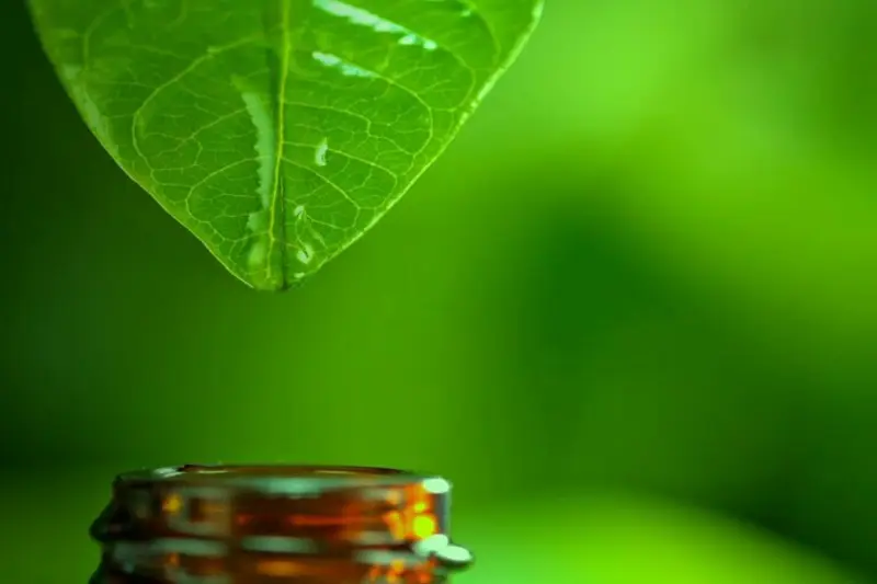 Golden drop of herbal extract falling from a leaf into an amber bottle